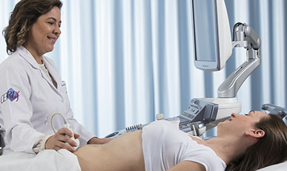 Profissional de saúde sorrindo realizando ultrassonografia na paciente deitada