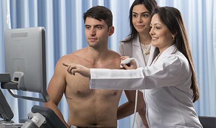 Profissionais de saúde apontando para um monitor explicando a ultrassonografia para o paciente
