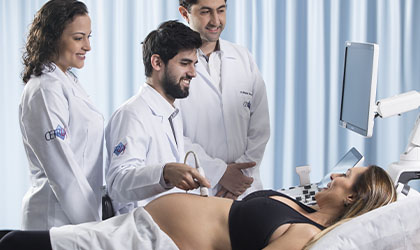 Três profissionais de saúde realizando ultrassonografia em uma gestante