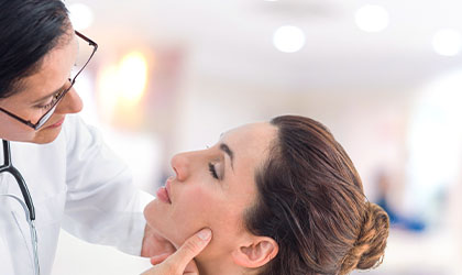 Profissional de saúde examinando a pele de uma paciente enquanto segura seu maxilar